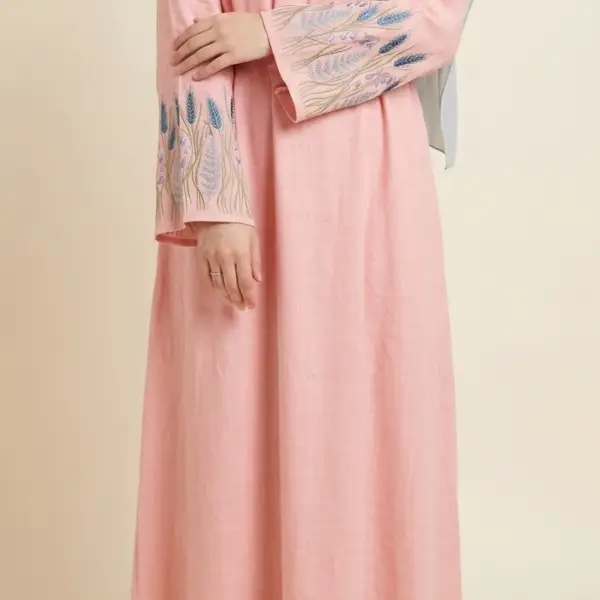 Front view of a Muslim hijabi model wearing a pink linen-viscose maxi dress featuring intricate blue and purple wheat and floral embroidery on the sleeve cuffs.