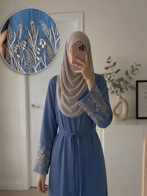 Front view of a blue linen-viscose muslim long dress featuring intricate floral embroidery around the neckline .