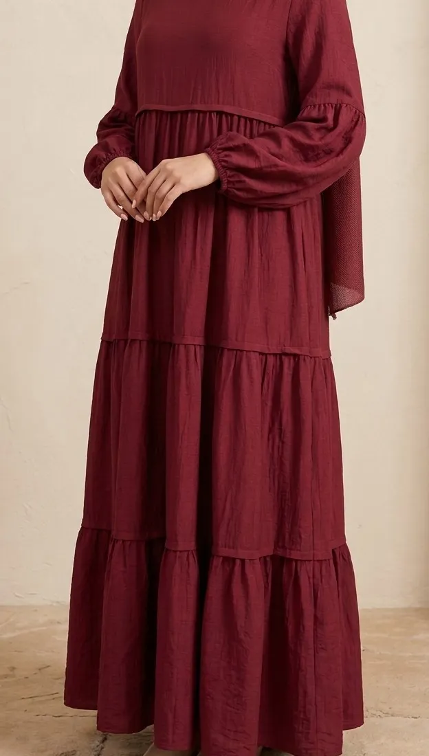 Front view of model wearing a burgundy red tiered maxi dress in a rayon-linen blend with long sleeves and a matching hijab from Hoor.